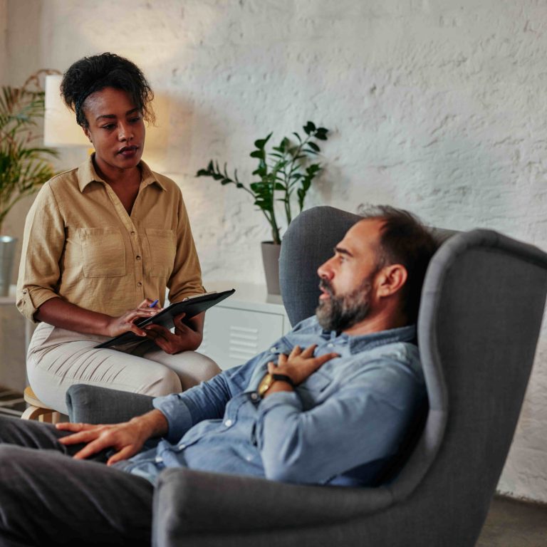 Frustrated middle age man sitting in armchair and solving his mental problems while having therapy session with african female psychologist