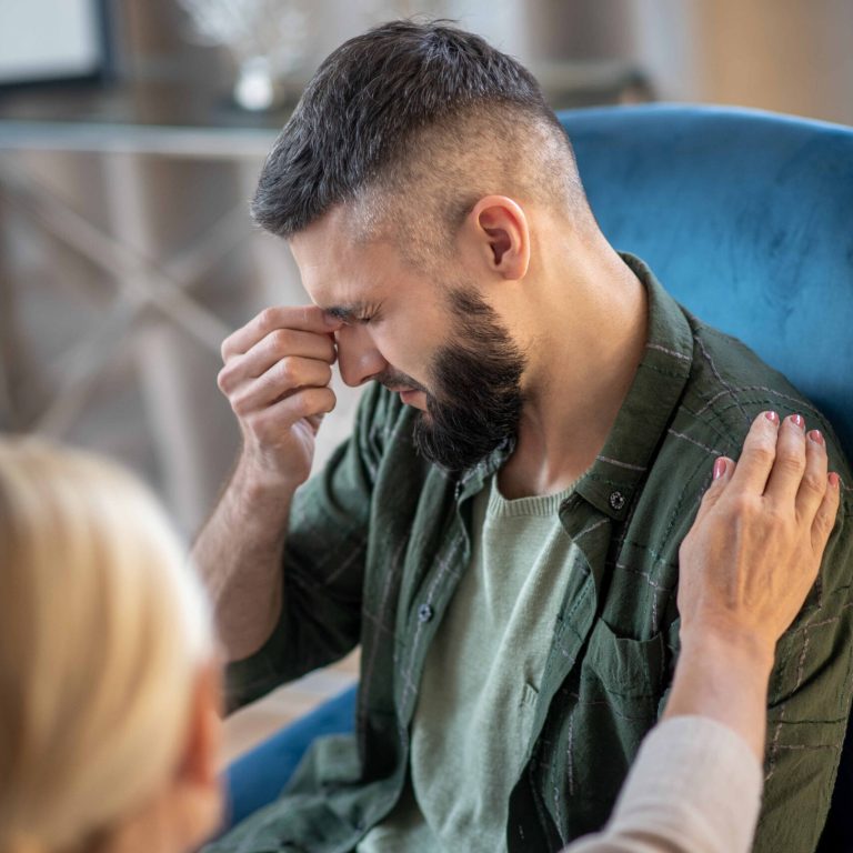 Supporting man. Blonde psychoanalyst supporting man having strong headache during talk